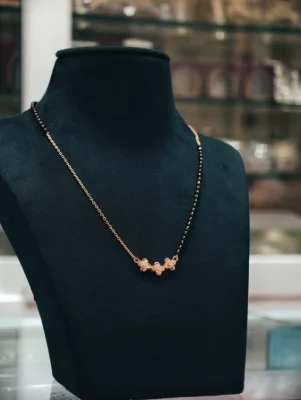 A delicate silver mangalsutra featuring a chain of black beads and a central locket with three small flower-shaped silver motifs.