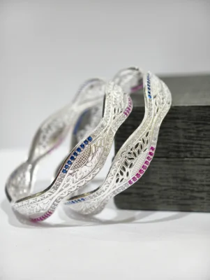 These wavy silver bangles feature intricate cutwork patterns accented with sparkling white, blue, and pink stones.
