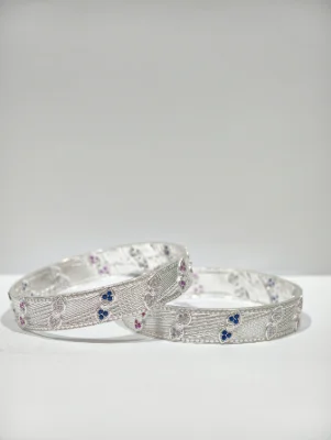 These round silver bangles feature a fine textured pattern with alternating blue and pink stone accents.