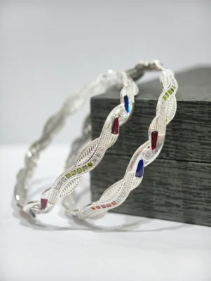 A pair of twisted silver bangles featuring a wave pattern with embedded multi-colored stones and clear accents.