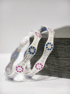 Silver bangles featuring wavy patterns with blue, pink, and white stones set in floral motifs.