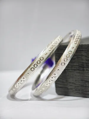 Silver bangles featuring textured patterns and circular motifs with a matte finish.