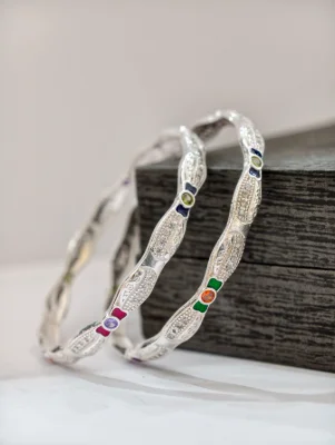 Silver bangles featuring wavy patterns, white stones, and colorful enamel accents.