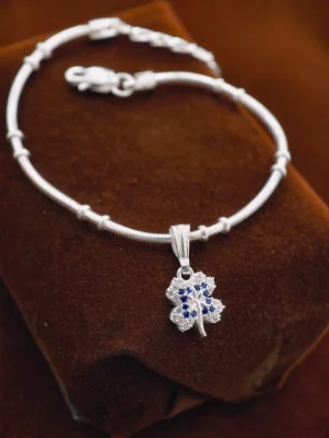A delicate silver chain bracelet featuring a four leaf clover charm set with small white and blue stones.