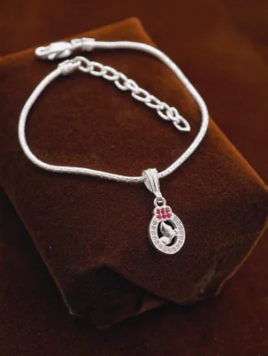 Silver chain bracelet with an oval pendant featuring small white stones, red stones, and a silver motif.