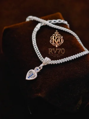 This silver chain bracelet features a delicate heart pendant embellished with blue and clear stones.