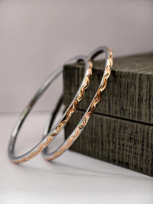 These simple silver bangles feature a shiny finish with a delicate engraved pattern along the outer edge.