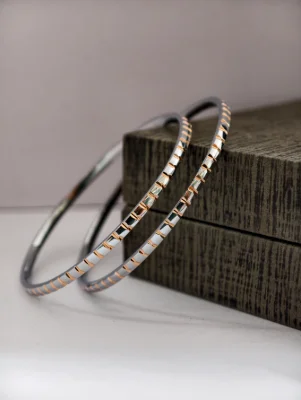 Pair of round silver bangles featuring a textured pattern with alternating polished silver and gold tone segments.