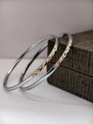These round silver bangles feature a textured matte finish with delicate golden leaf motifs along the top.