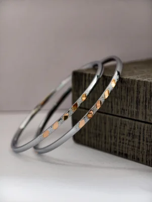 Pair of round silver bangles featuring a textured finish and alternating polished diamond shaped patterns.