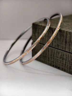 Pair of round silver bangles featuring a dual tone chevron pattern with silver and copper colors.