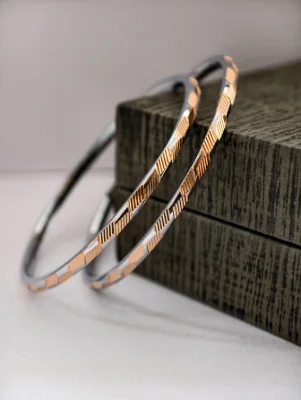 A pair of round silver bangles featuring a textured dual tone finish with diagonal grooves on the surface.