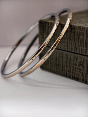 A pair of round silver bangles featuring a smooth finish with a central band of subtle gold-toned embossed dots.