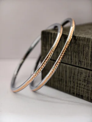 These simple silver bangles feature a glossy finish and a central row of small golden dots.