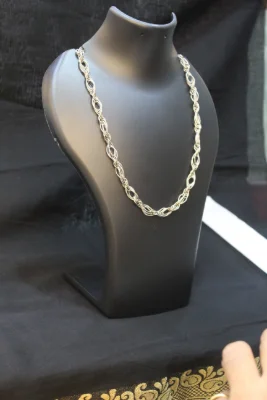 A silver chain with interconnected twisted loop patterns, featuring a polished finish and elegant metallic shine.