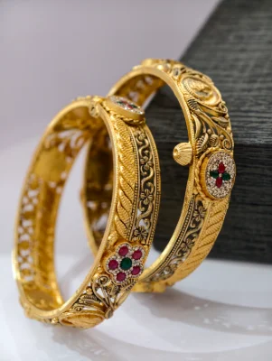 A pair of gold polished silver kadas featuring intricate floral patterns and colourful stones set in a detailed antique finish.