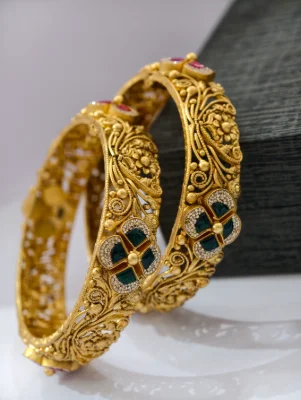Gold polished silver kadas featuring intricate floral filigree patterns accented with green stones.