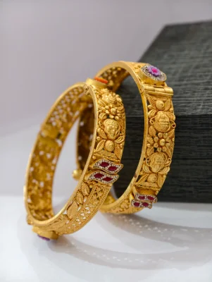 Gold polished silver kada with intricate floral carving, traditional motifs, and colourful stone accents.