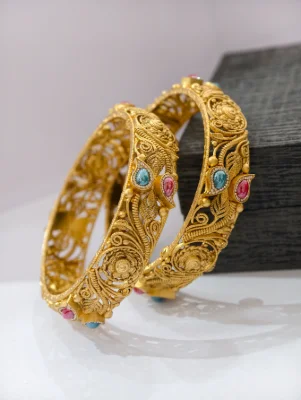Gold polished silver kadas featuring intricate floral filigree patterns adorned with colorful stones.