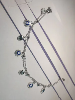 A delicate silver bracelet featuring double chains with hanging evil eye charms, stone studded hearts, and small beads.