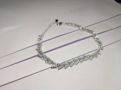 A shiny silver bracelet featuring sparkling white stones set in an interlocking zig zag design with an adjustable chain.