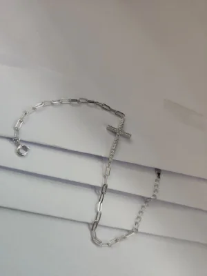 A light silver bracelet featuring a link chain design adorned with a stone studded cross pendant and secure clasp.