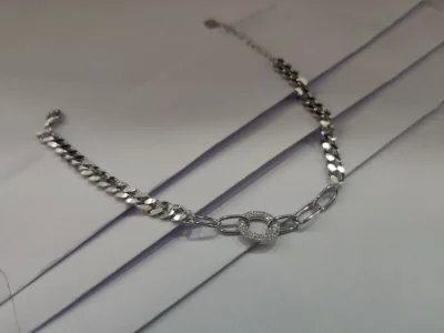 Silver bracelet with curb chain links and a center ring charm paved with white stones.